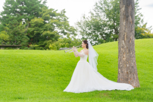 鮮やかな芝生の丘でトランペットを奏でる新郎新婦